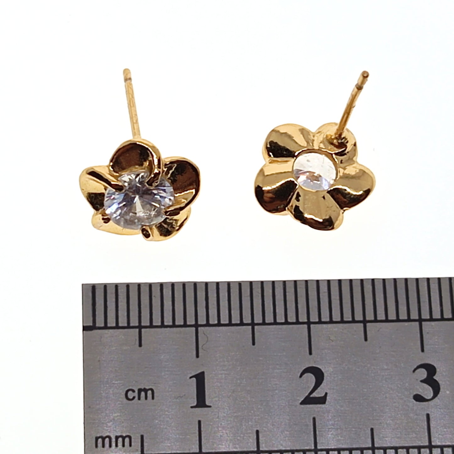 Gold flower-shaped earrings with embedded stones on a ruler for scale.