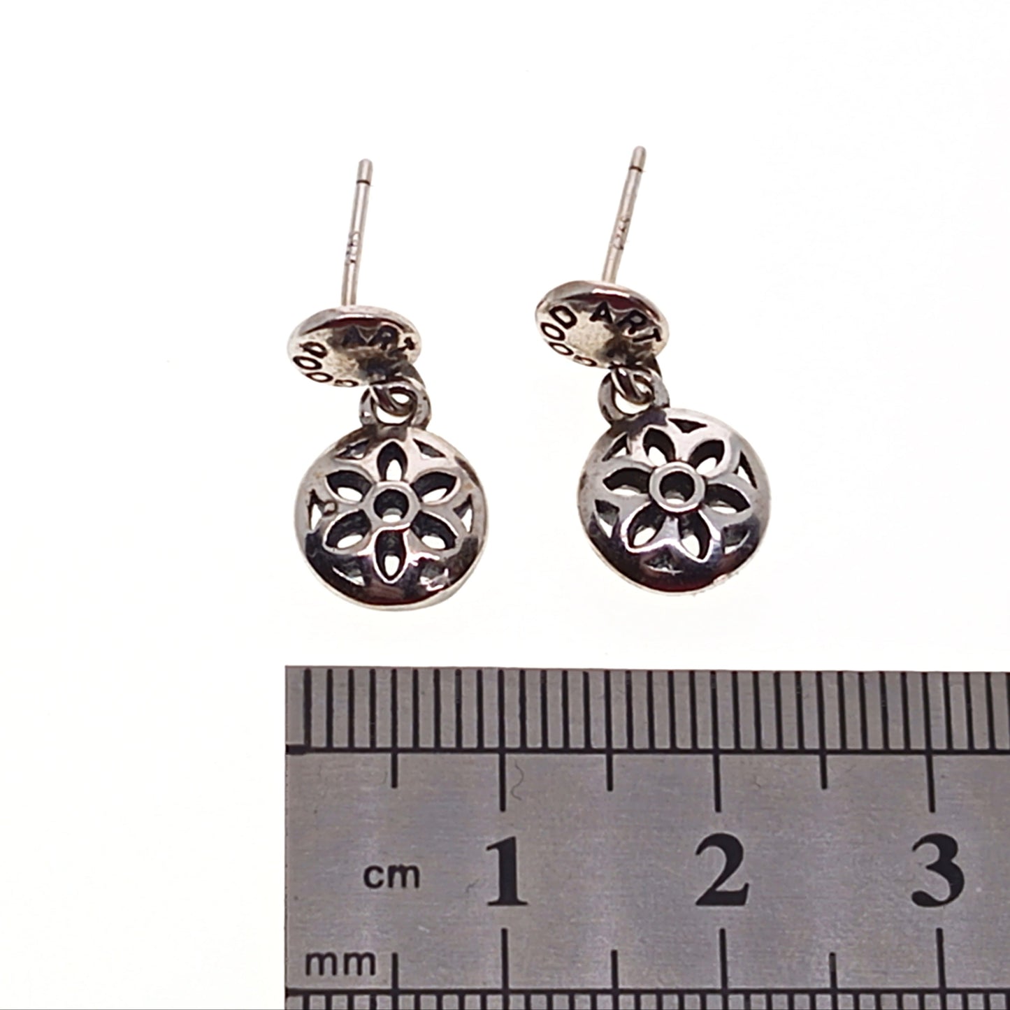 Silver earrings with floral design on a white background, next to a ruler for scale.