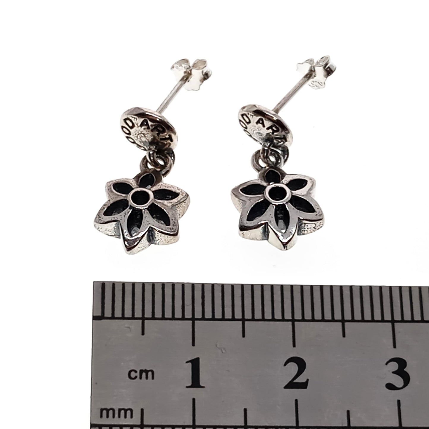 Silver flower-shaped earrings with a ruler for scale on a white background