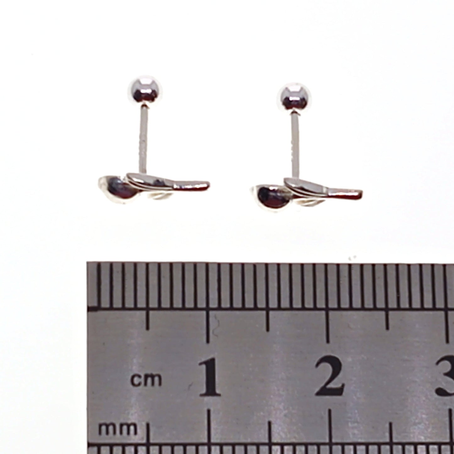 Pair of silver earrings with a ruler for scale on a white background
