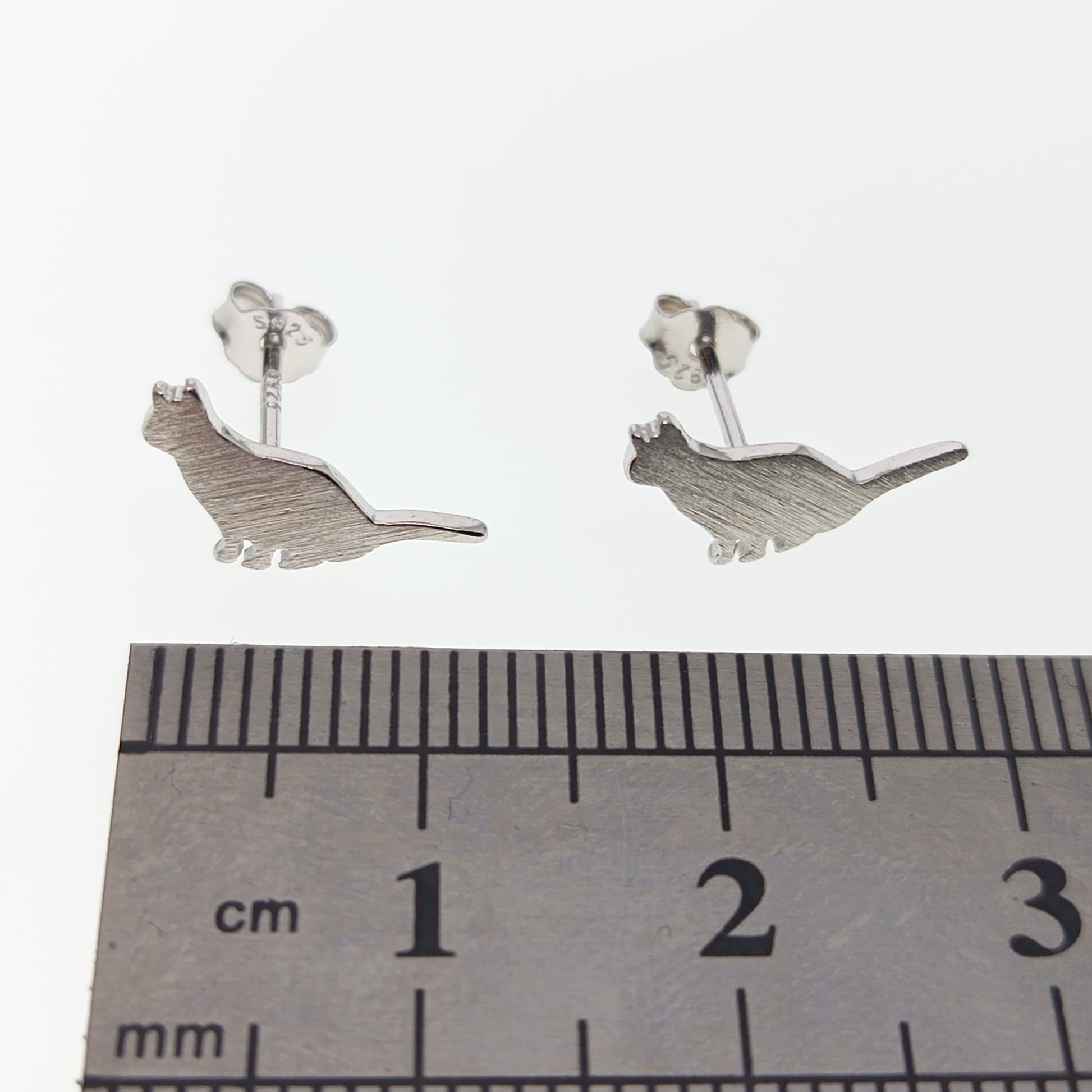 Silver cat-shaped earrings on a white background with a ruler for scale.