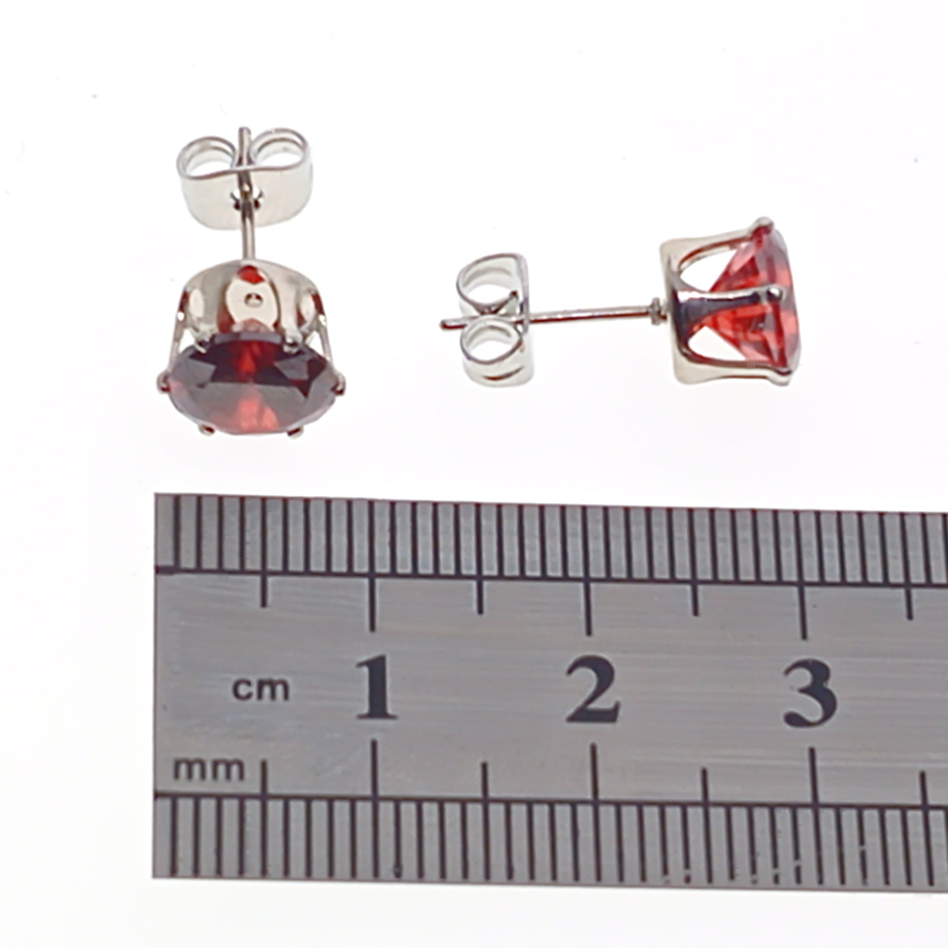 Silver earrings with red gemstones next to a ruler for size reference on a white background