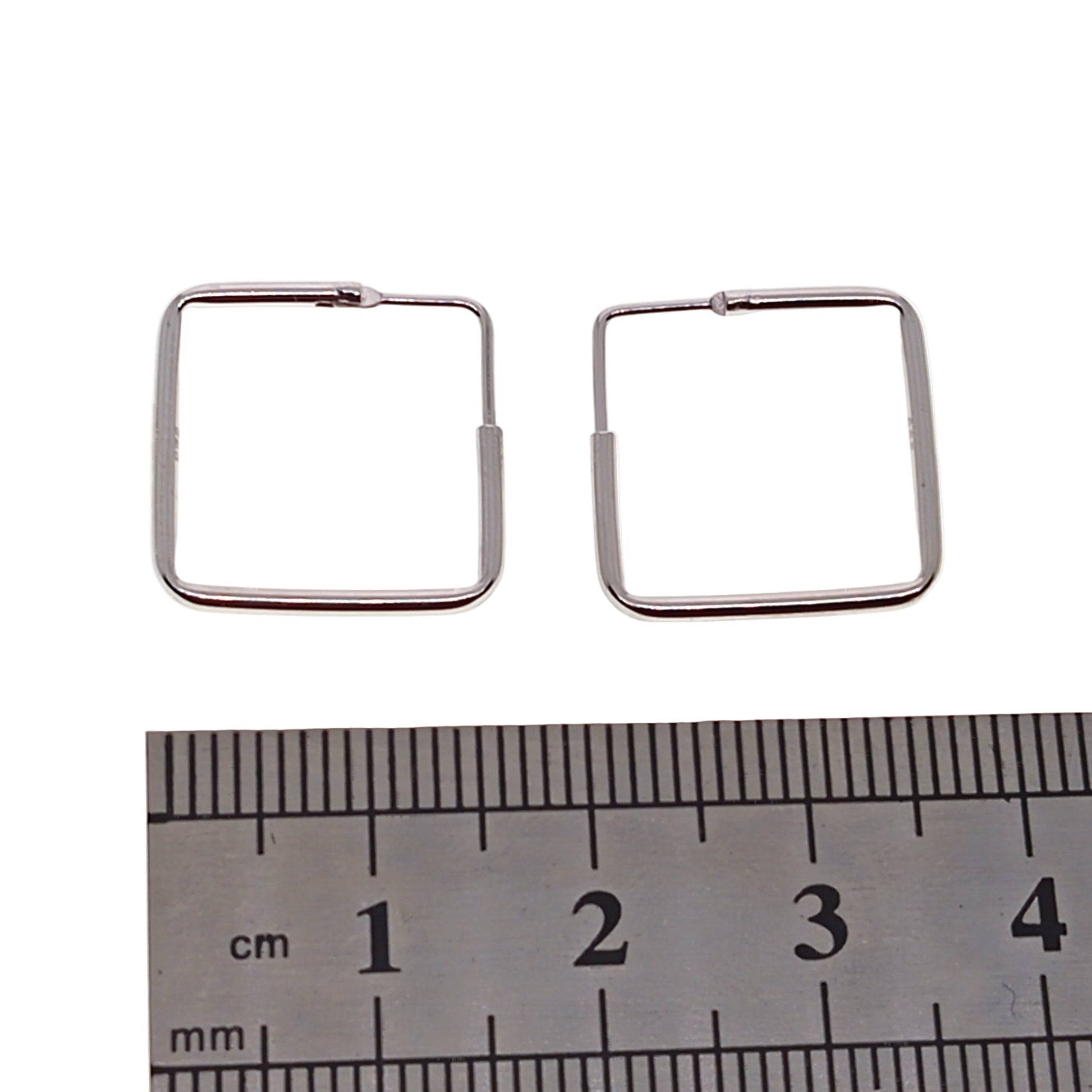 Silver square hoop earrings with a ruler for scale on a white background