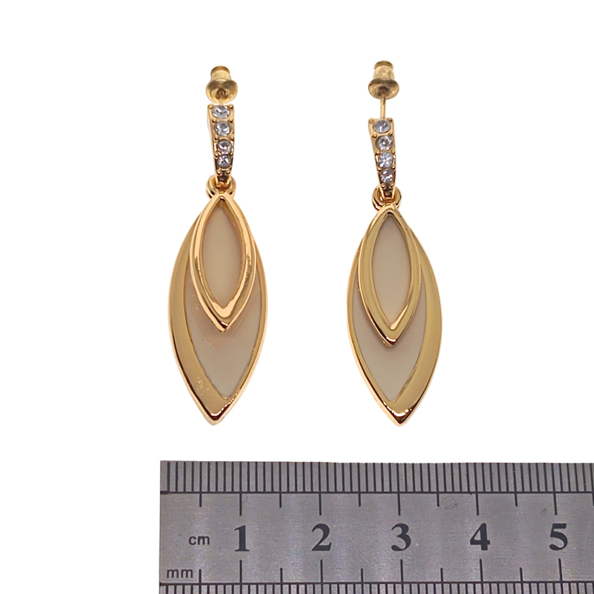 Gold and white earrings with a ruler for scale on a white background
