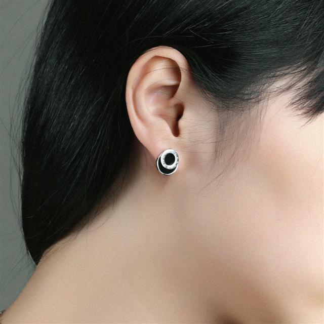 Close-up of an ear wearing a black and silver earring against a neutral background
