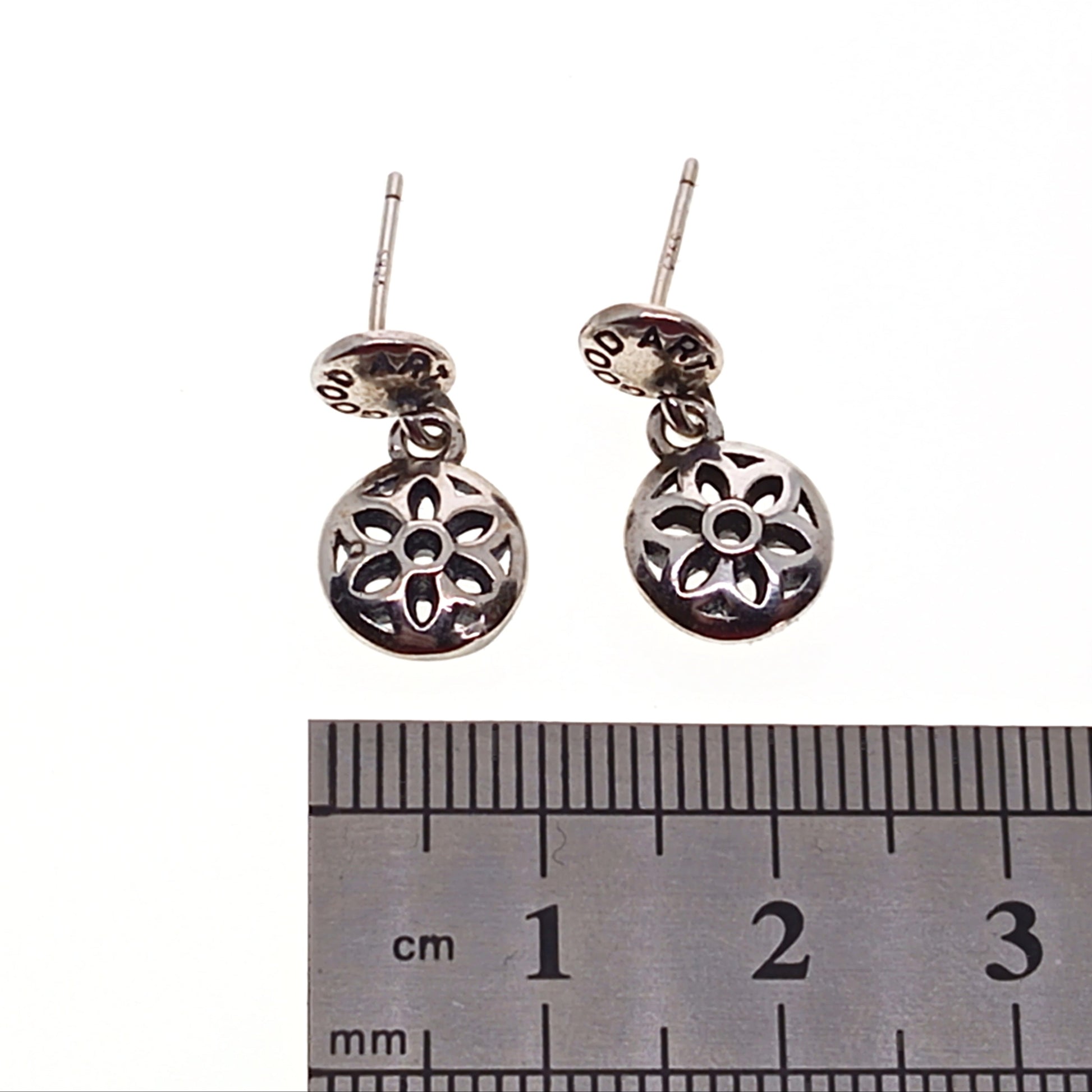 Silver earrings with floral design on a white background, next to a ruler for scale.