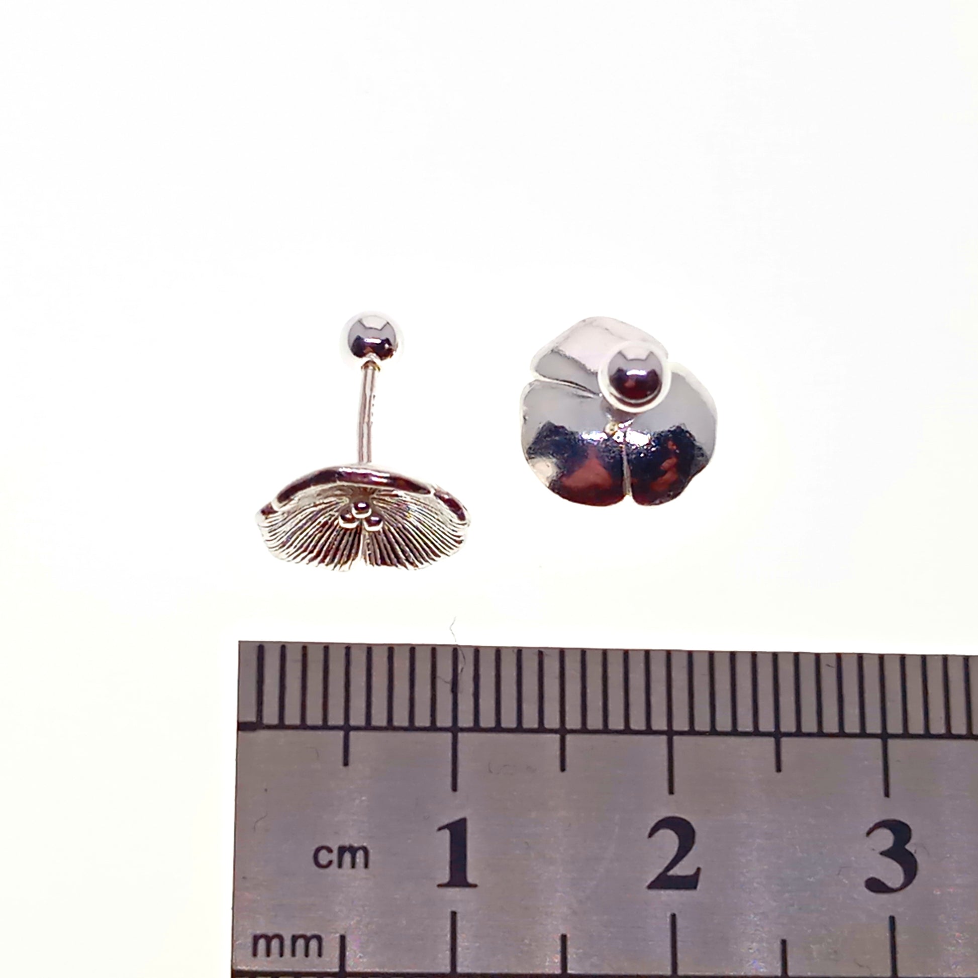 Pair of silver earrings with a central gemstone, shown next to a ruler for scale.